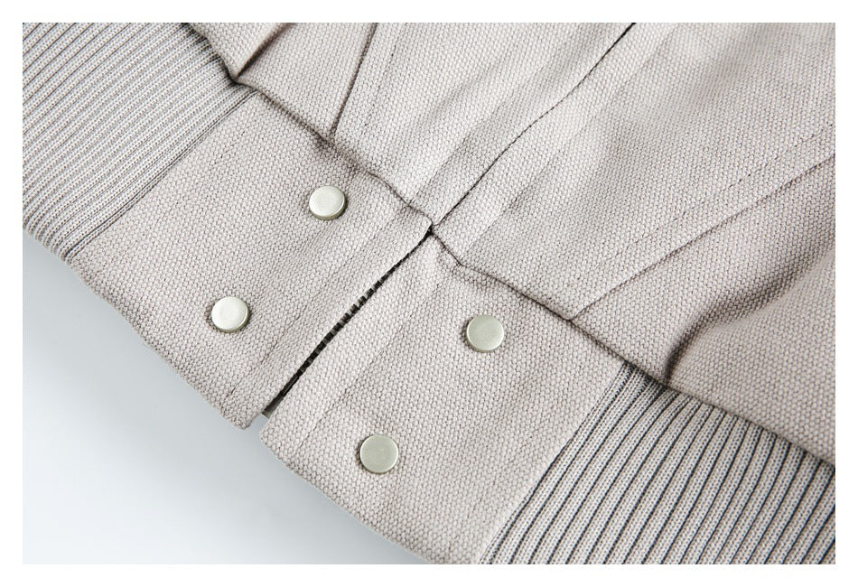 Close-up of a jacket's ribbed edges and pale taupe-gray fabric, with several silver snap buttons.