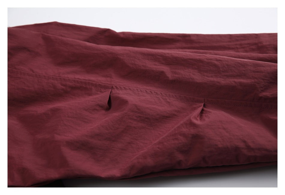 Close-up of burgundy garment fabric with a horizontal seam and gathered folds.