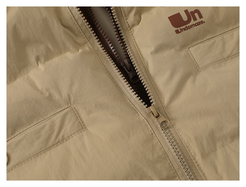 Close-up of a beige jacket with an open zipper, flap pockets, and a brown chest logo.
