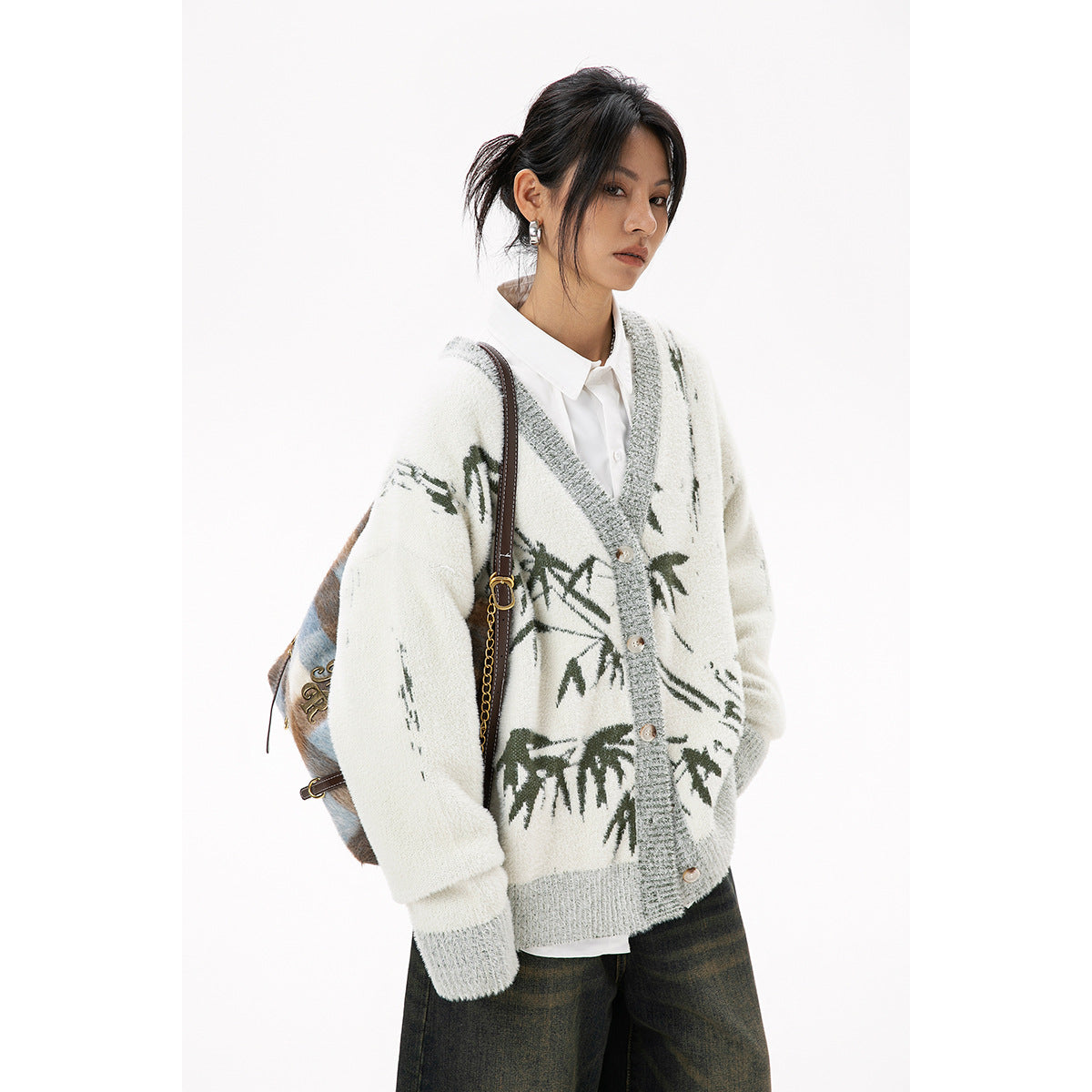 Model wearing an ivory button-front cardigan with gray ribbed trim and dark green abstract botanical motifs.