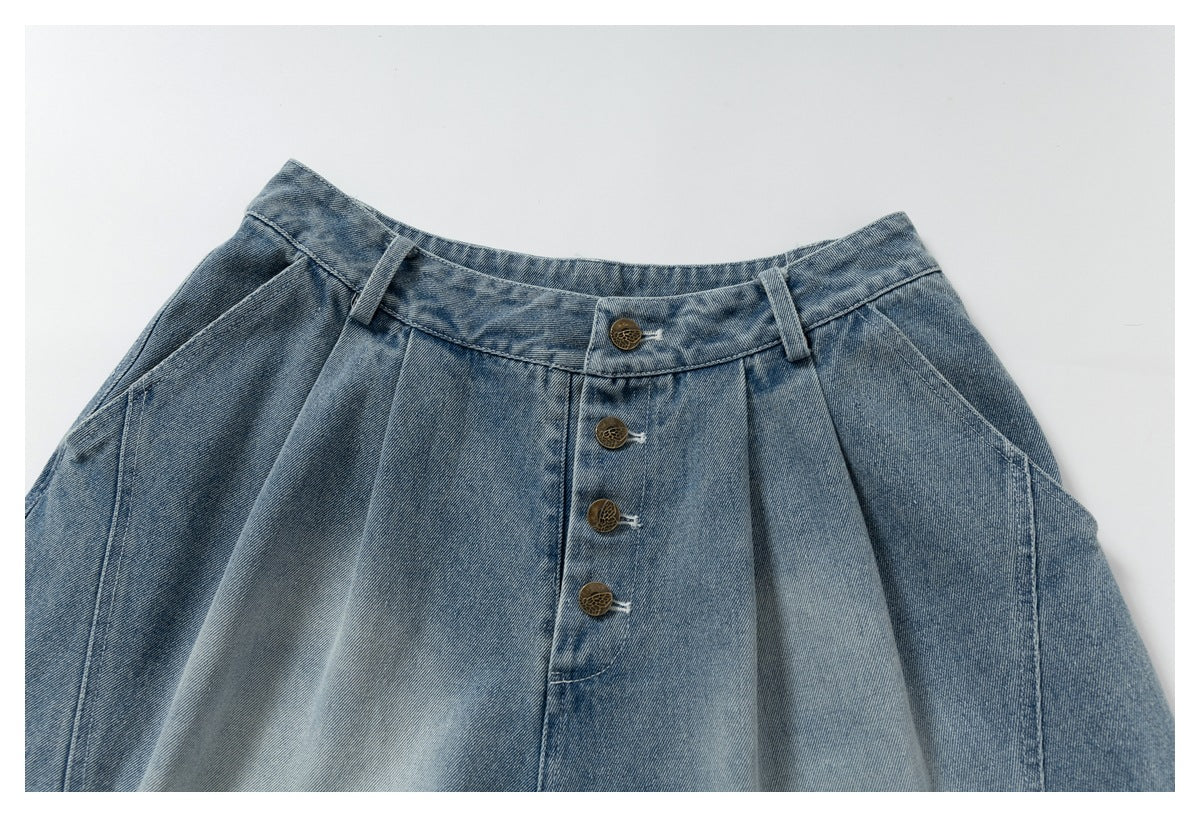 Close-up of the front waistband and pleats of blue denim trousers with four brass-tone buttons.