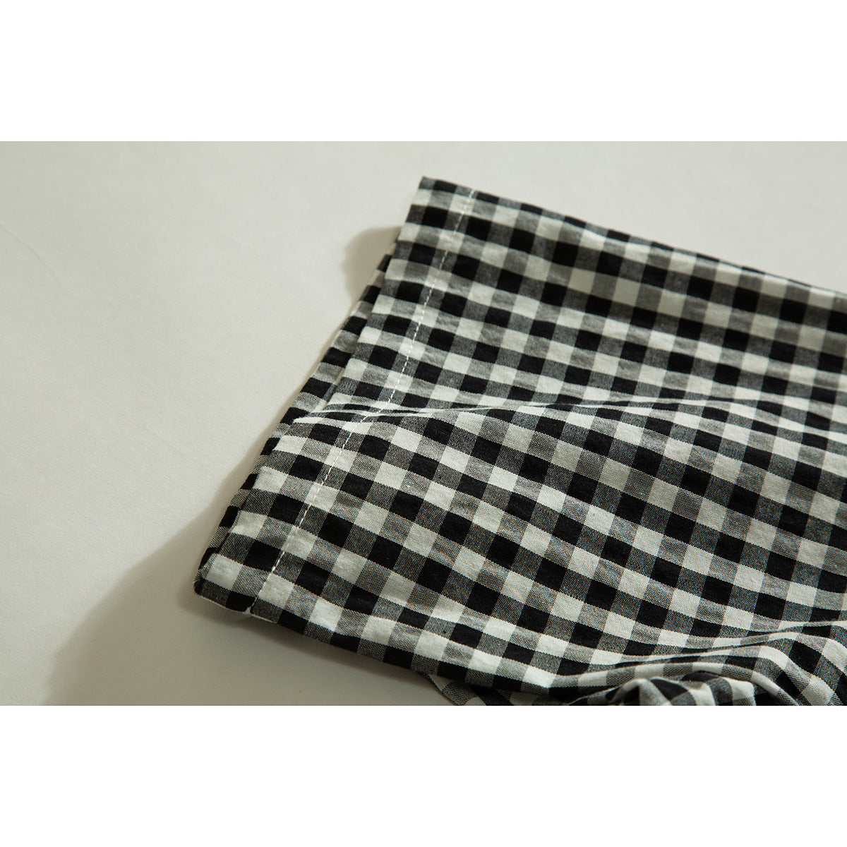 Close-up of a folded section of black-and-cream checked shirt fabric and stitched edge.