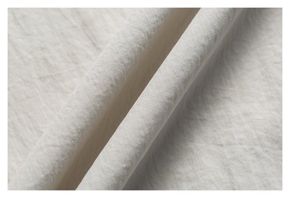 Close-up of light gray-beige garment fabric folded to show its fine woven surface.
