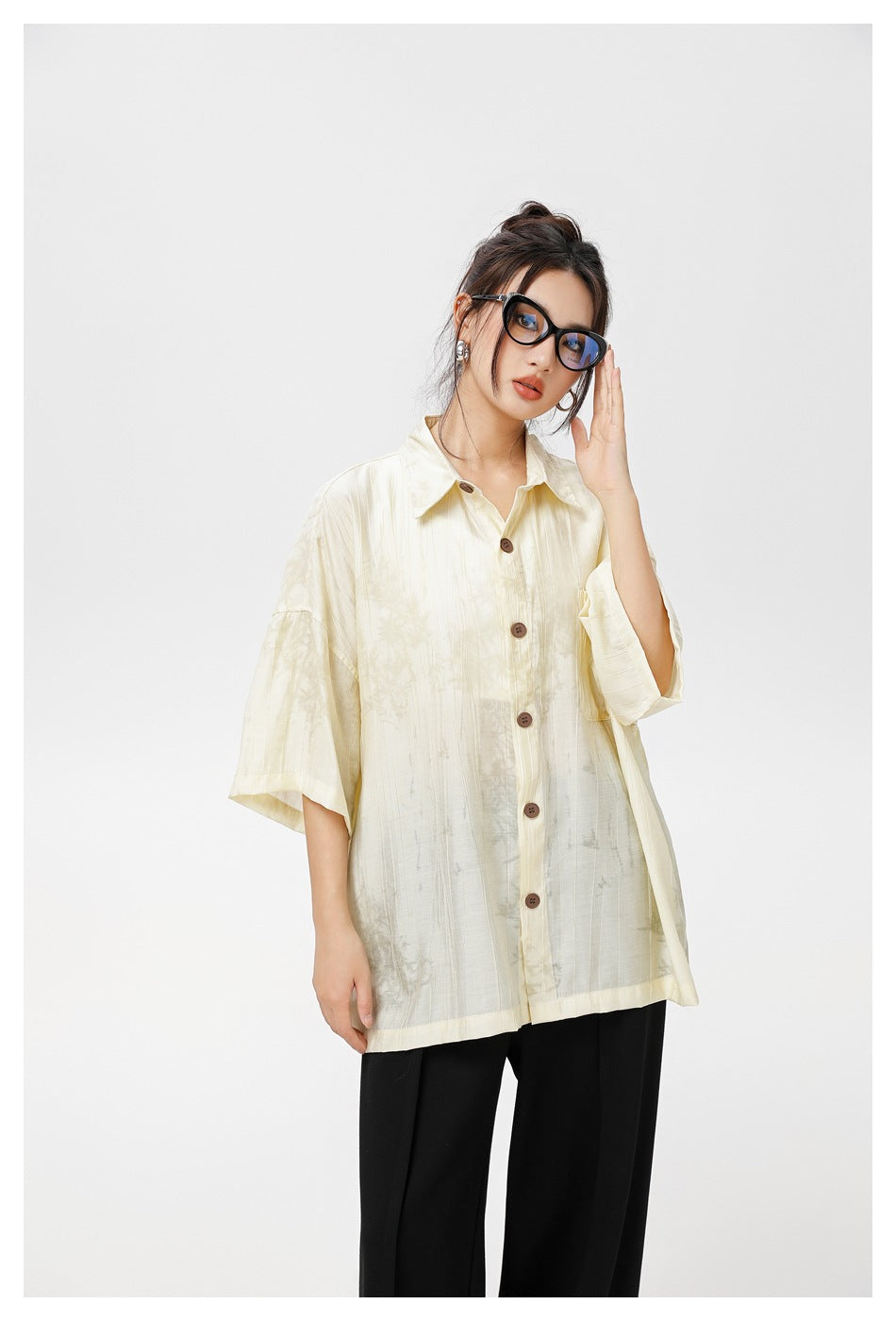 Model wearing a loose ivory short-sleeve button-up shirt with subtle gray patterning and black trousers.