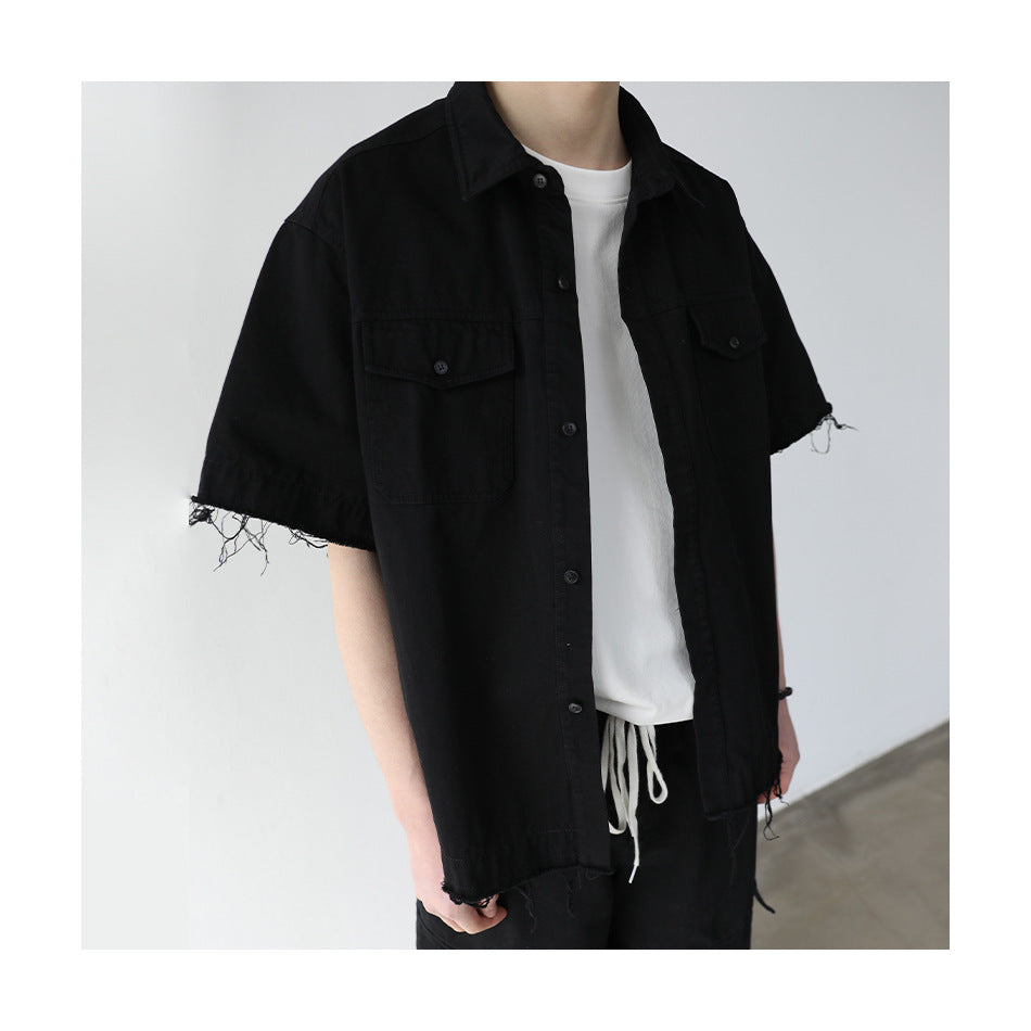 Model wearing a black short-sleeve button-up shirt with two flap chest pockets and frayed sleeve and hem edges.