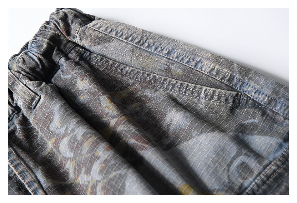 Close-up of the gathered waistband and pocket stitching on dark gray plaid trousers.