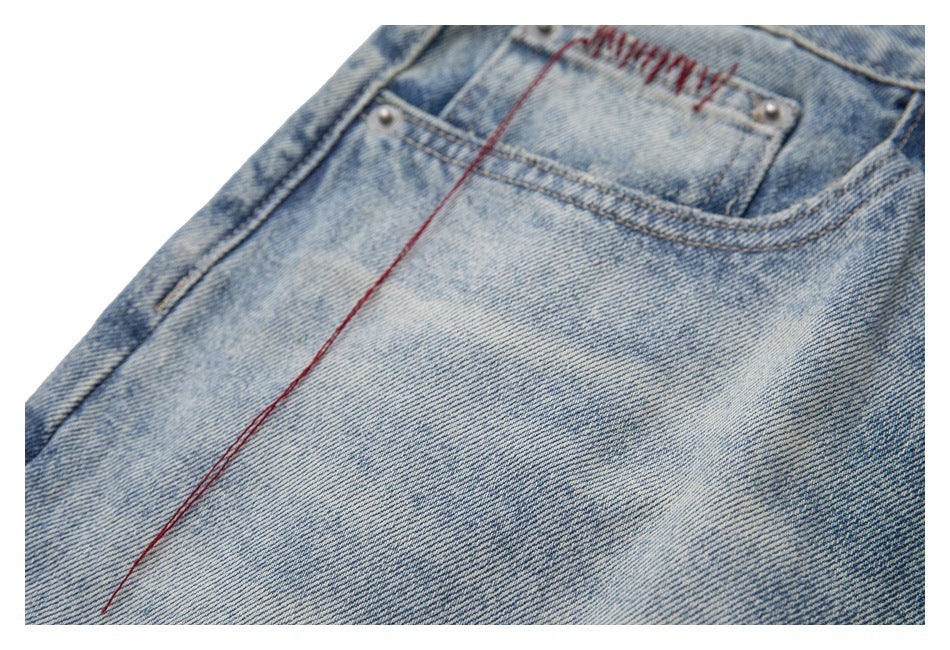 Angled close-up of faded blue denim with a front coin pocket and a long loose red thread.