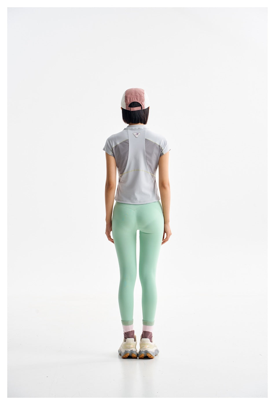Rear view of a model wearing a light gray color-block top and mint leggings.