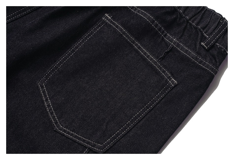 Close-up of a black denim garment with a large back pocket and contrasting double-stitched seams.