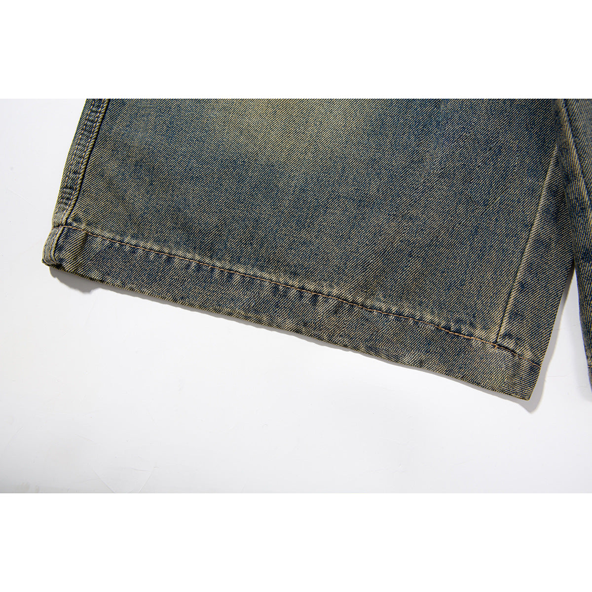 Close-up of the wide hem and contrast stitching on blue-brown washed denim shorts.