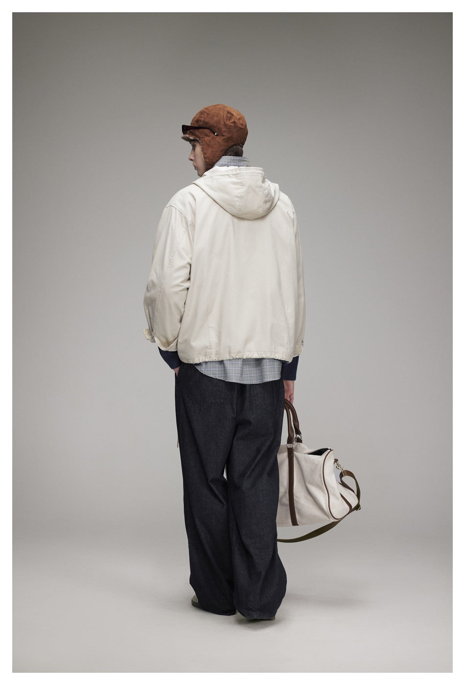 Rear view of a model wearing an off-white hooded jacket and dark wide-leg trousers, carrying a cream bag.