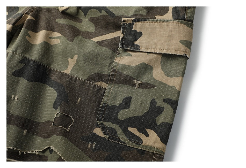 Close-up of a buttoned cargo pocket and distressed fabric on olive, brown, and tan camouflage shorts.