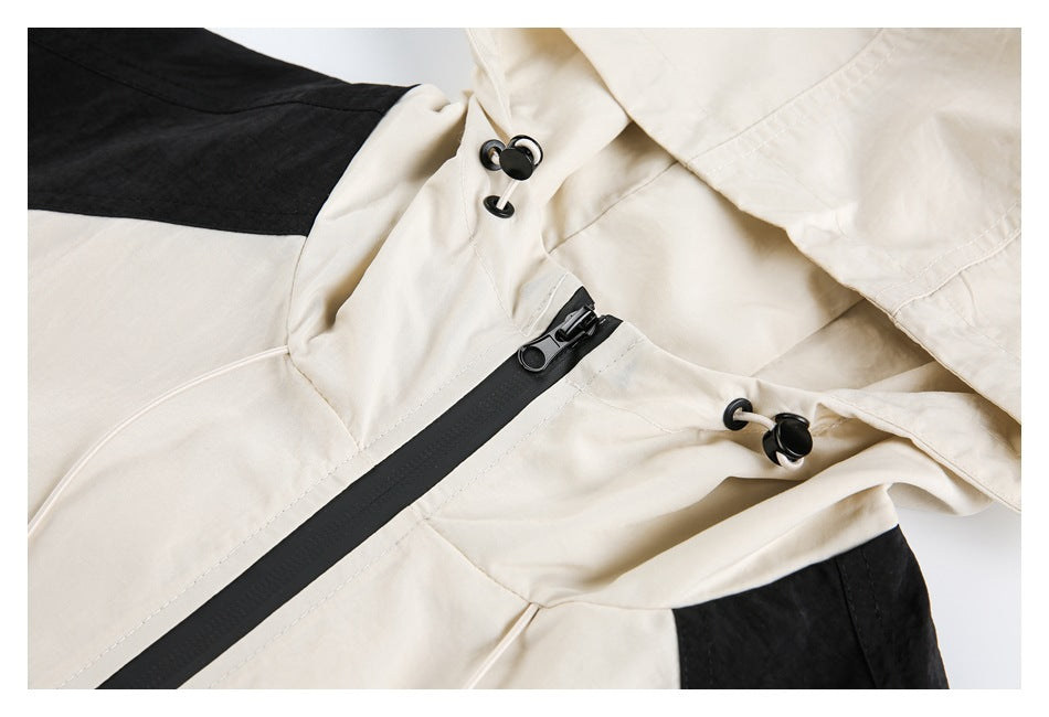 Close-up of a cream jacket's hood, black zipper, and drawcord toggles, with a black shoulder panel visible.