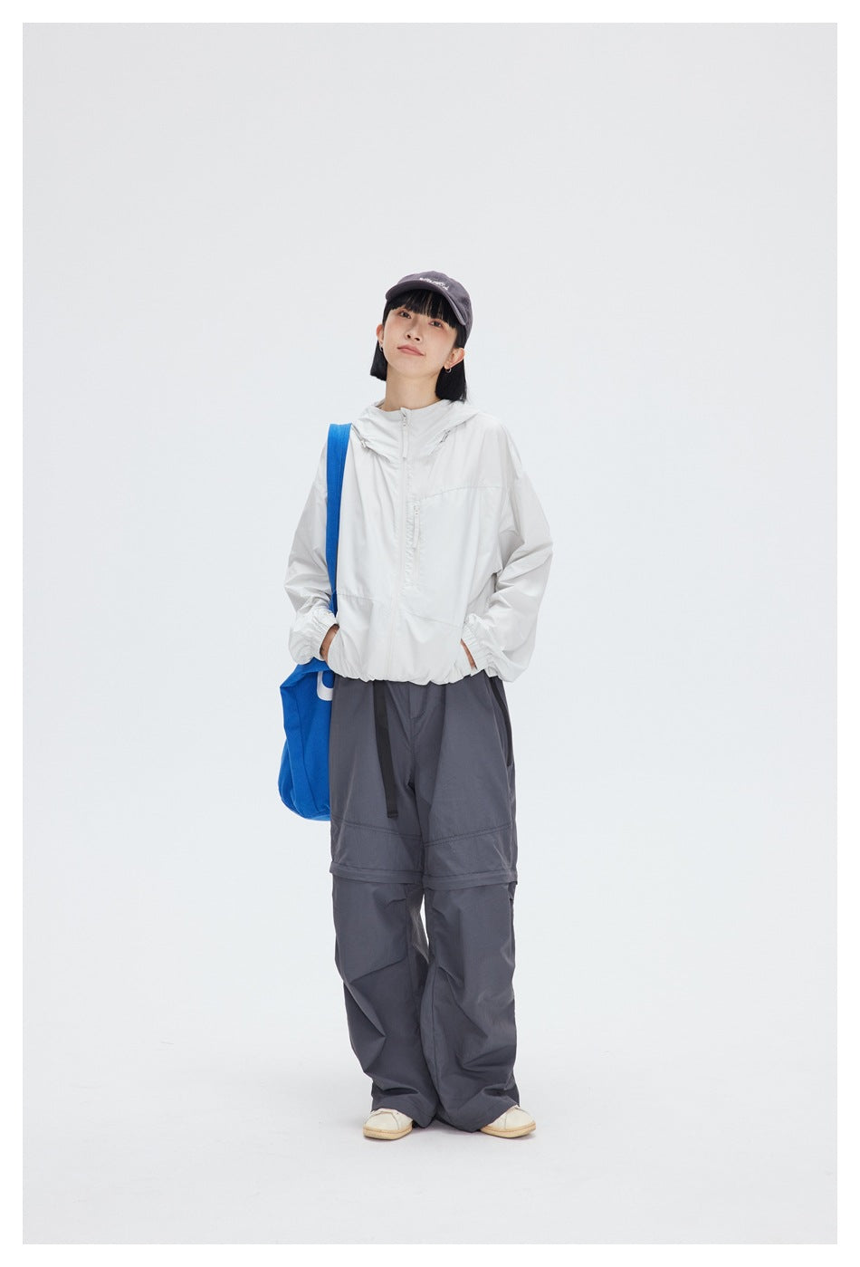 Full-length view of a model wearing a white hooded jacket and loose charcoal-gray trousers.