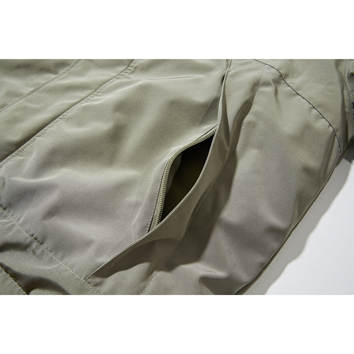 Close-up of a khaki jacket’s zippered pocket, seams, and surrounding panels.