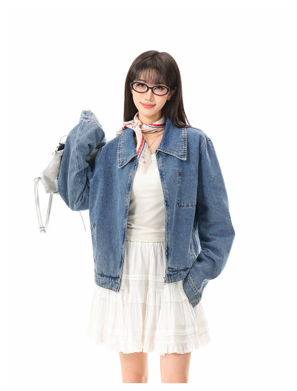 Close-up of model in blue denim zip jacket with collar, chest pocket and white skirt, one arm raised holding a bag