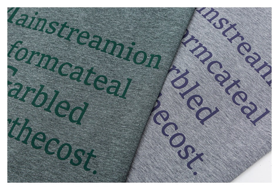 Close-up of green and light gray heathered shirts with oversized dark English text printed on the fabric.