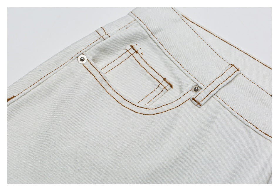 Close-up of the small coin pocket, rivets, and tan stitching on the white jeans.