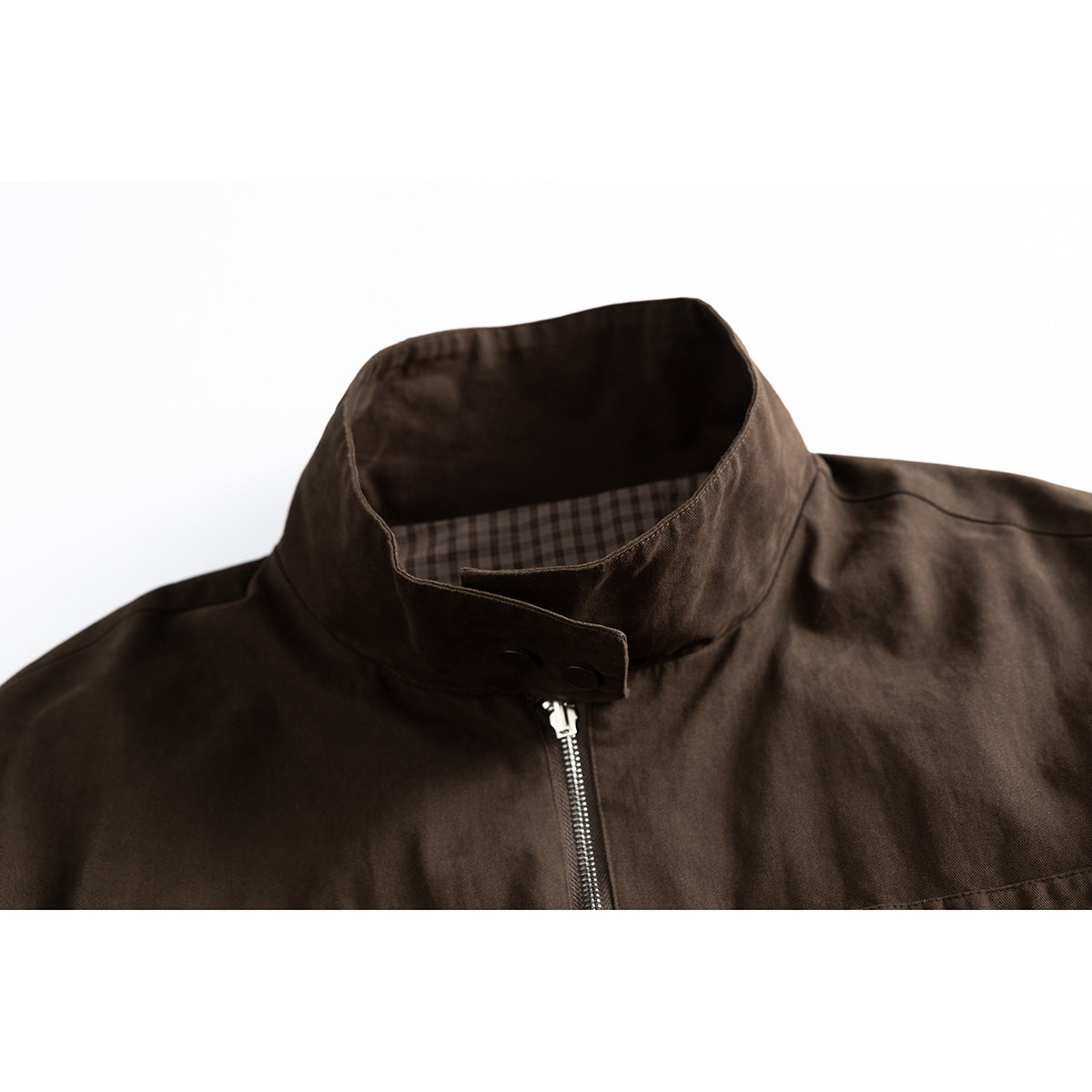 Close-up of a dark brown jacket’s stand collar, snap tab, front zipper, and checked inner collar lining.