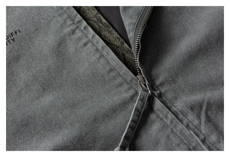 Close-up of a dark gray garment's zipper and seam, with partial black lettering printed on the fabric.