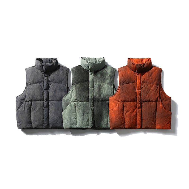 Three sleeveless quilted vests displayed together in charcoal gray, muted green, and rust orange.