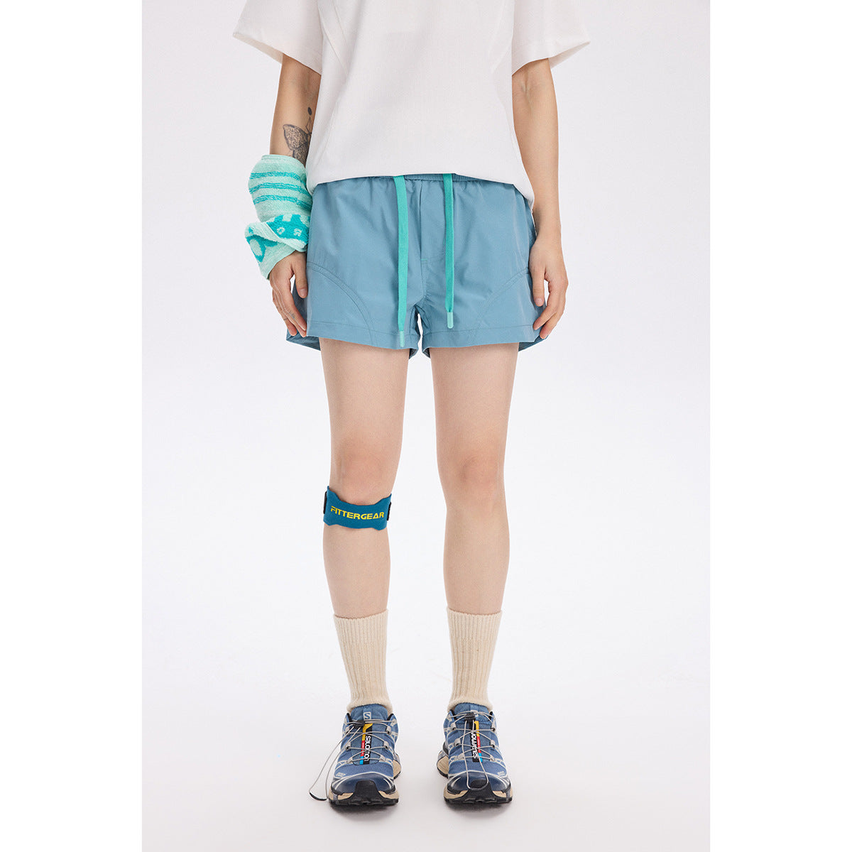 Model facing forward in light blue shorts with turquoise drawstrings and curved pockets, paired with a white top.
