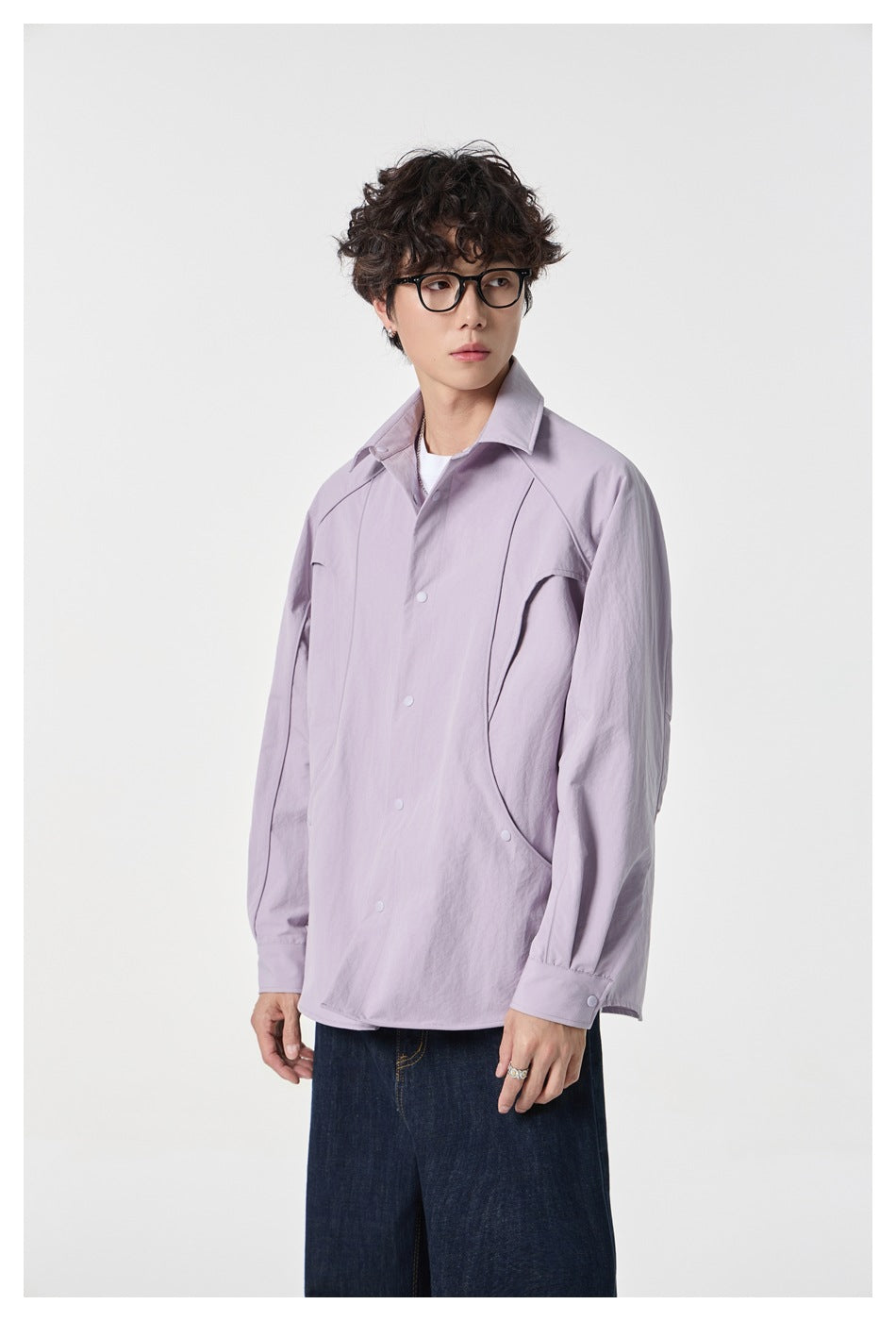 Model wearing a pale lavender snap-front shirt with curved panel seams and dark wide-leg jeans.