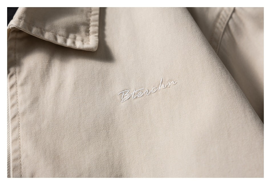 Close-up of white script embroidery on the chest of a beige jacket.