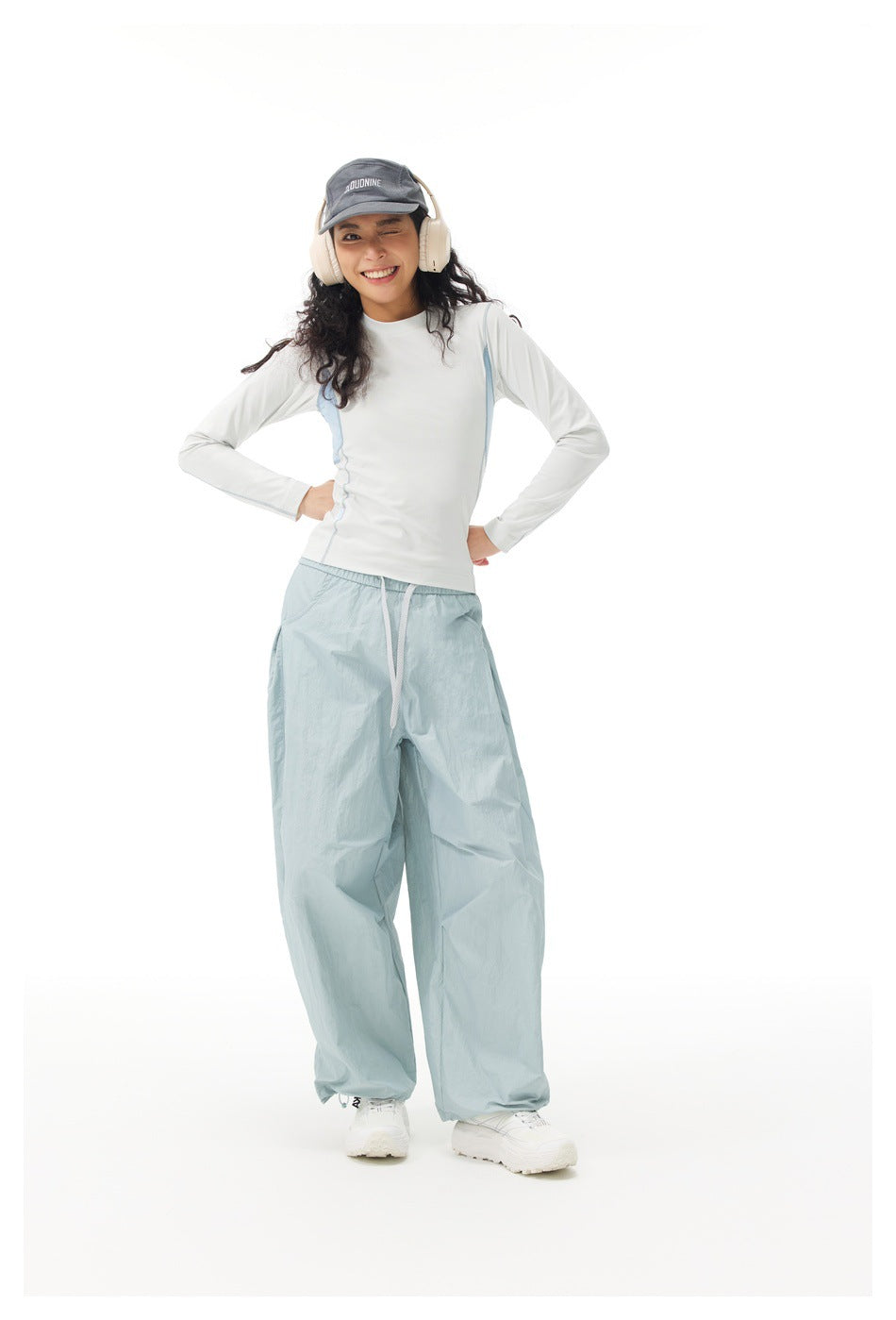 Person wearing a white long-sleeve top with light blue side panels, hands on hips, with light blue pants
