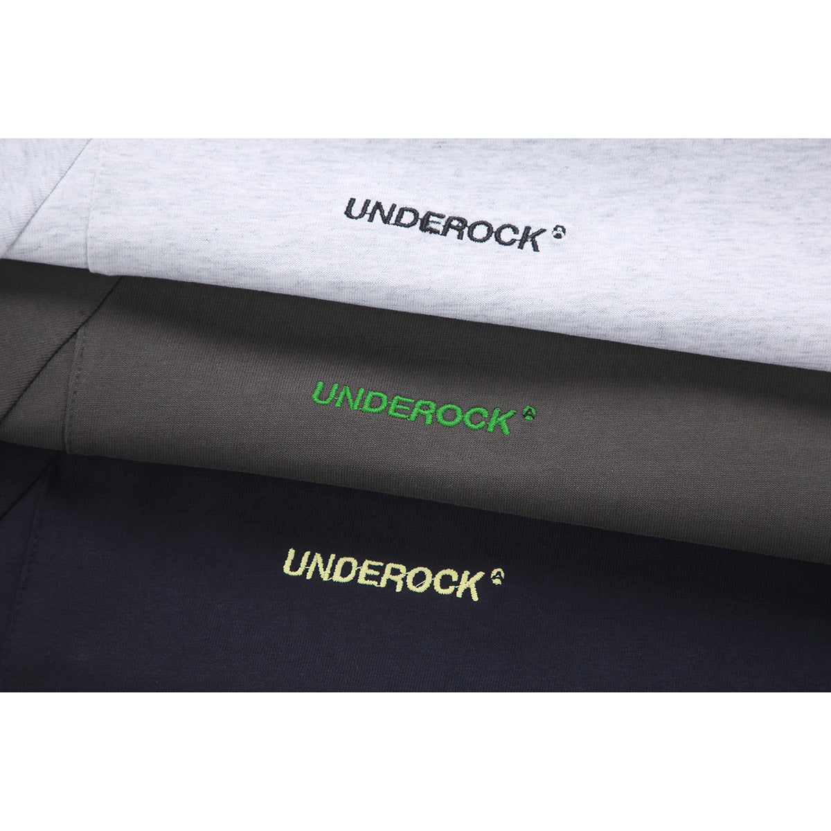 Three folded T-shirts in light gray, charcoal, and navy, each showing an embroidered chest logo.