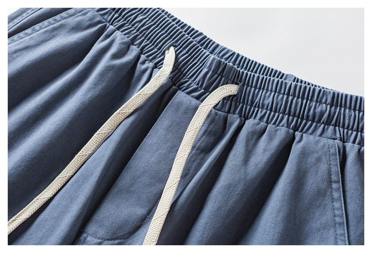 Close-up of blue pants showing the gathered elastic waistband, cream drawstrings, and front pockets.