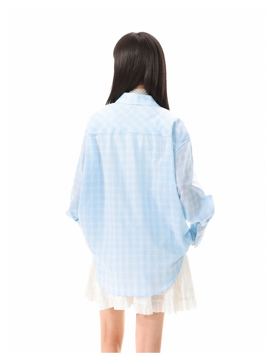 Back view of a model wearing an oversized light blue windowpane-check shirt over a white skirt.
