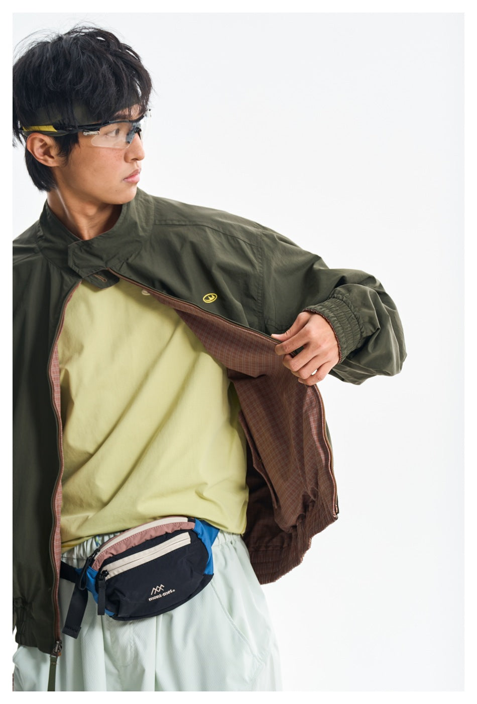 Model wearing an olive green jacket open to show its brown plaid lining and a pale yellow shirt.