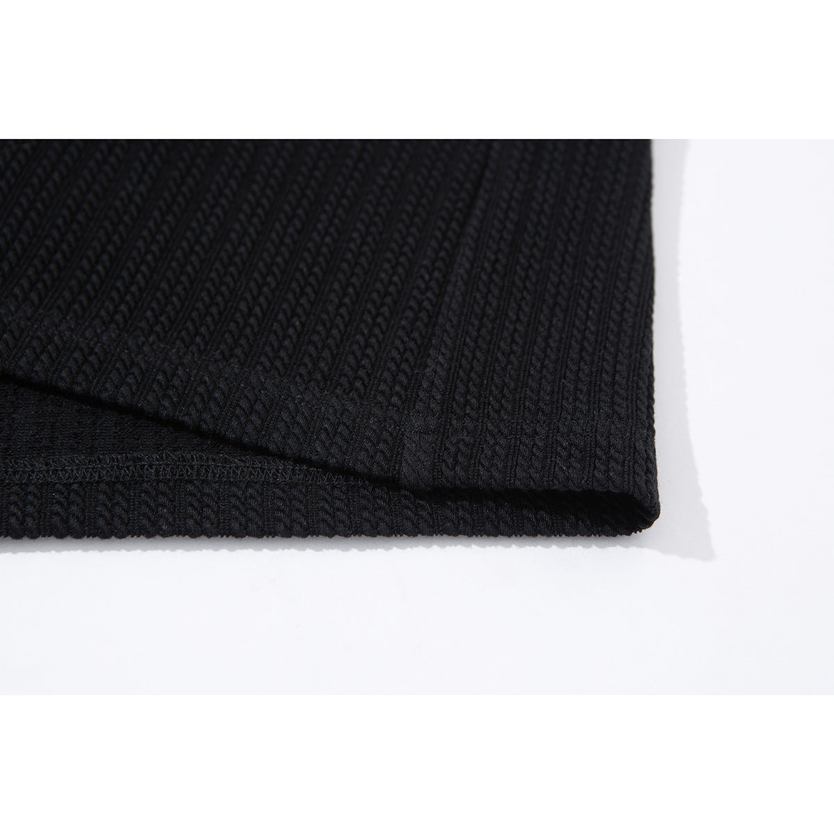 Close-up of the black ribbed shirt's folded hem and stitching on a white background.