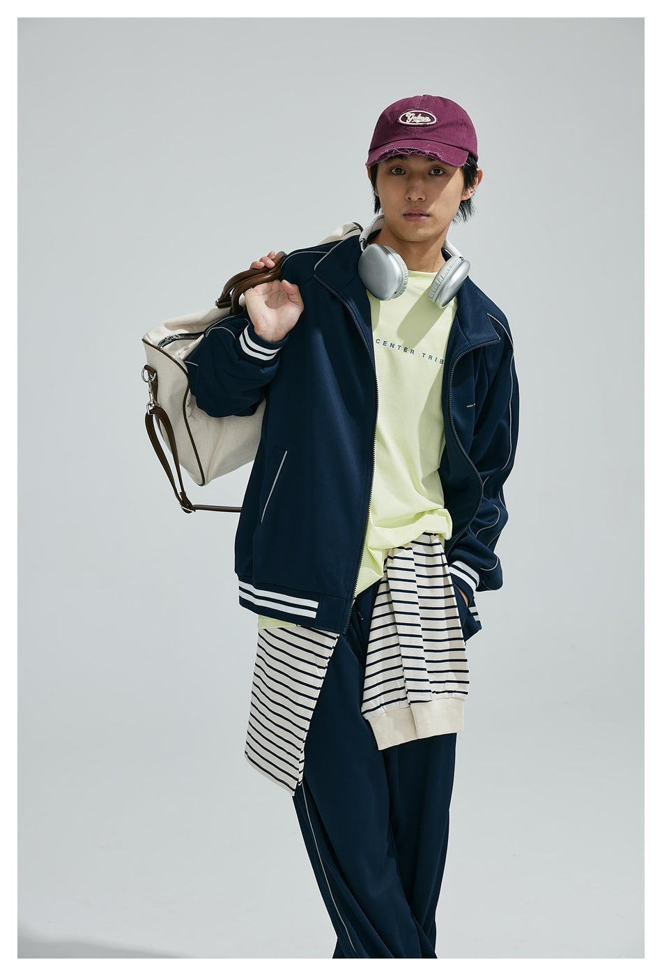 Model wearing a navy track jacket with white piping and striped trim over a pale yellow shirt.