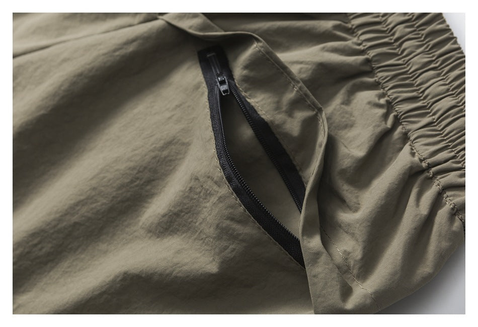 Close-up of a black zipper pocket beside the gathered waistband on a taupe garment.