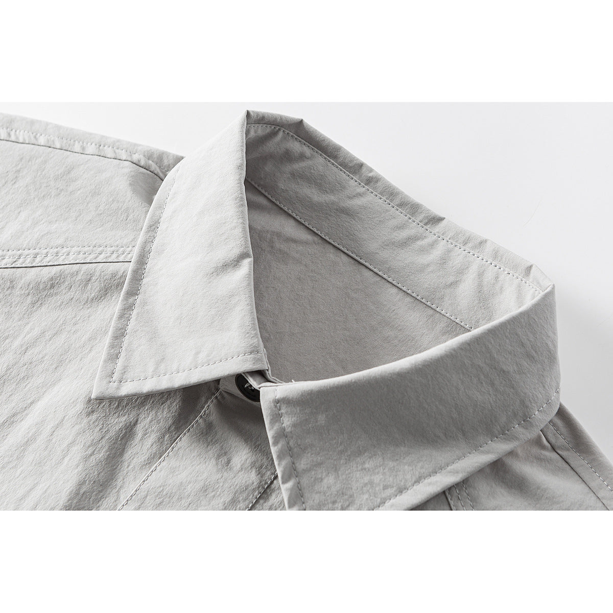 Close-up of a light gray shirt's pointed collar, stitching, and top button.