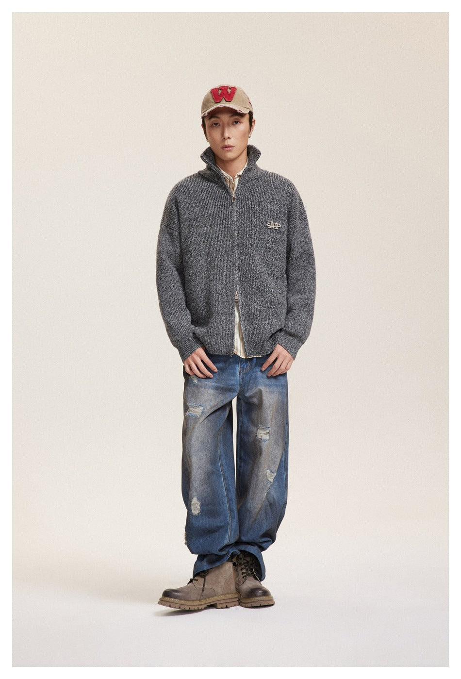 Front view of a model wearing a charcoal textured zip-up cardigan with a raised collar and loose distressed blue jeans.