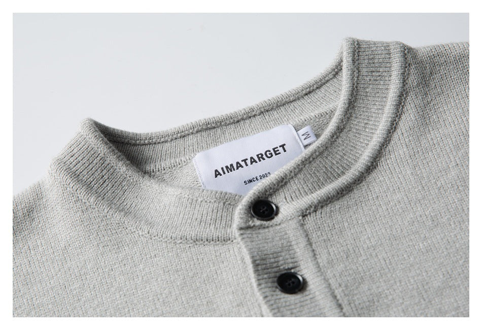 Close-up of a light gray knit sweater's ribbed band collar, black buttons and sewn neck label.