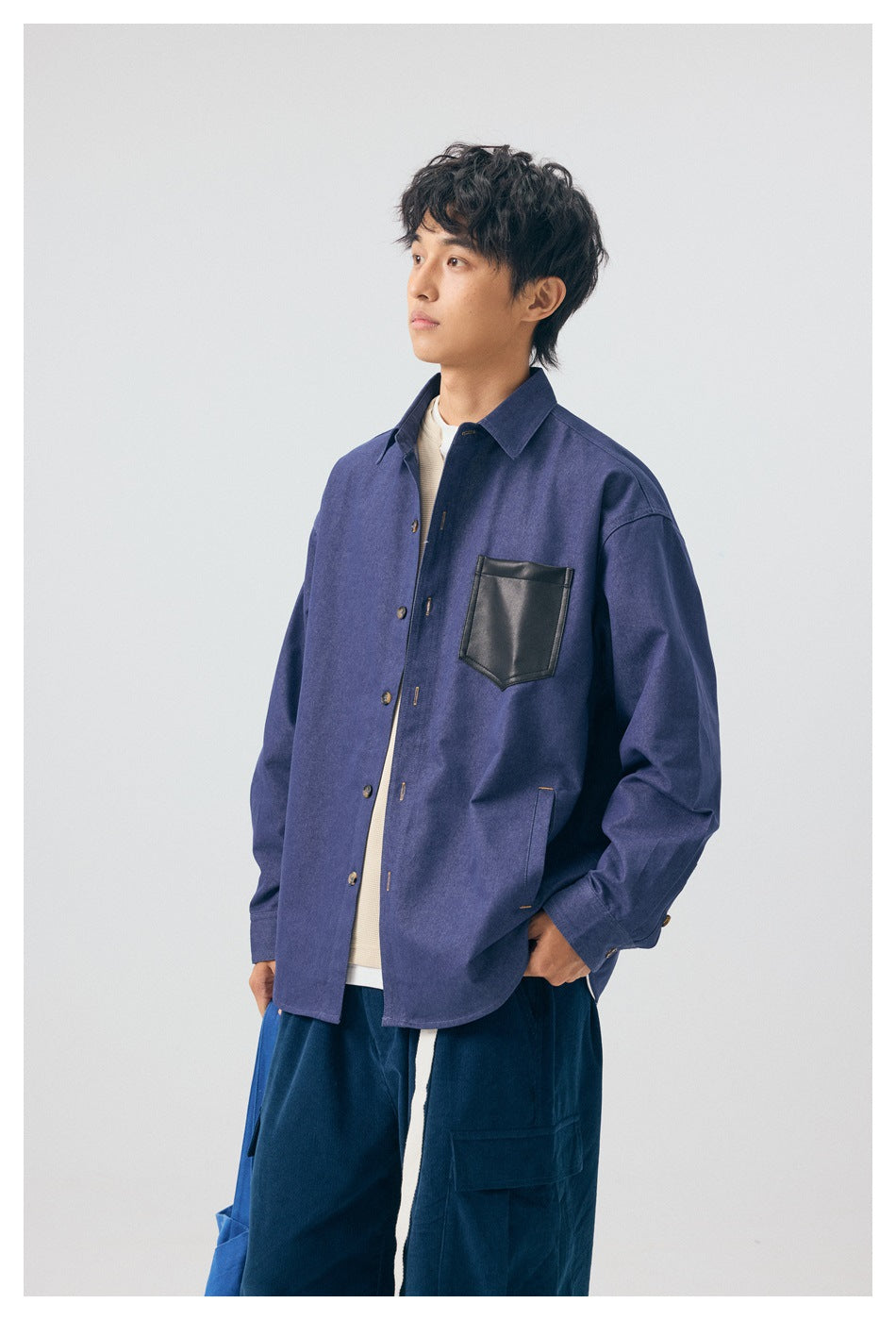 Model wearing a blue button-front overshirt with a black chest pocket, layered over a cream top.