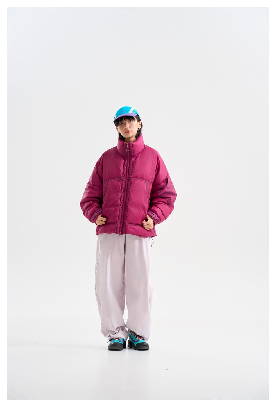 Front view of a model wearing a magenta puffer jacket with a high collar and pale wide-leg trousers.