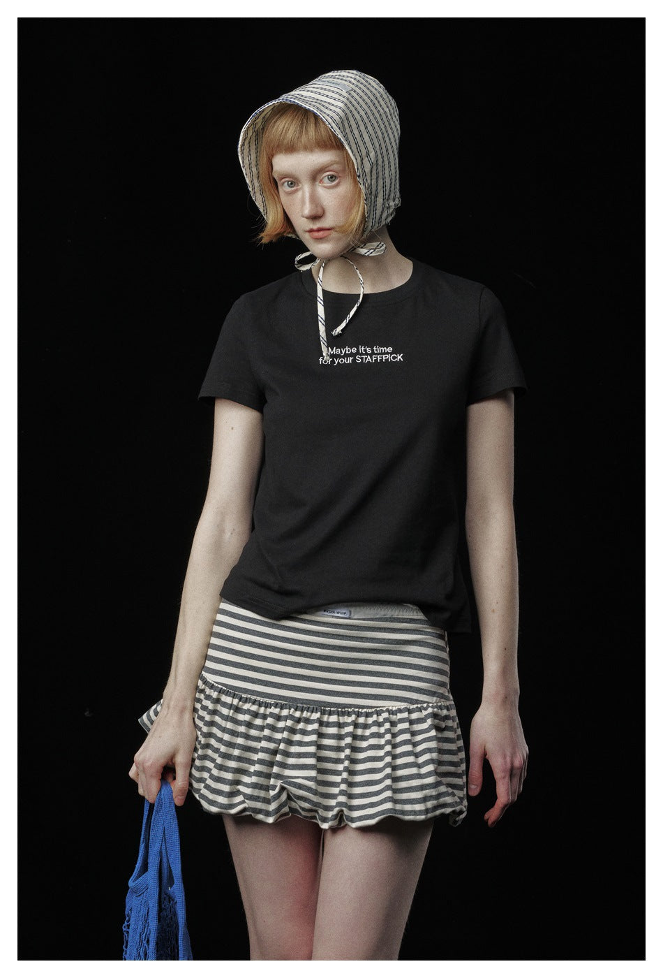 Model wearing a black short-sleeve T-shirt with small English chest text and a gray-and-white striped ruffle skirt.