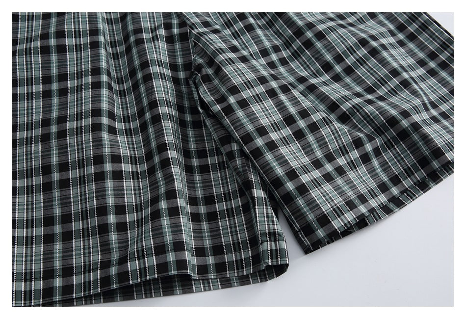 Close-up of the draped plaid trouser legs and stitched hems in black, gray, and muted green.