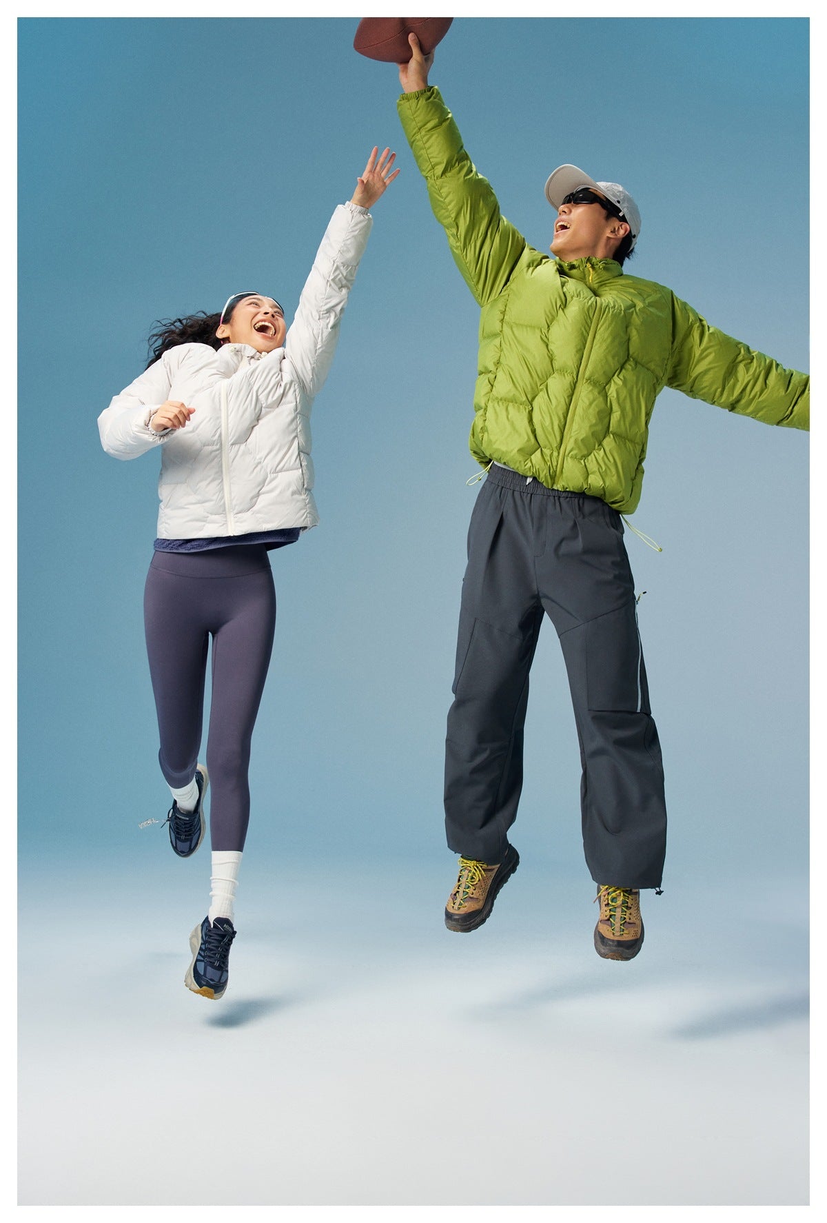 Two models in white and lime-green quilted jackets reach upward while playing with a ball.