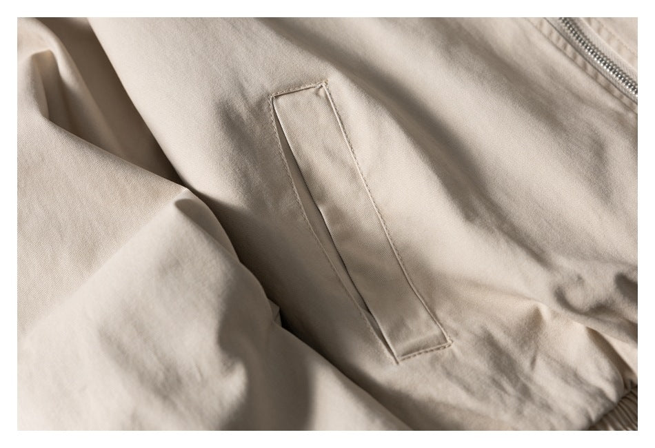 Close-up of a beige jacket's vertical welt pocket and a section of the zipper.