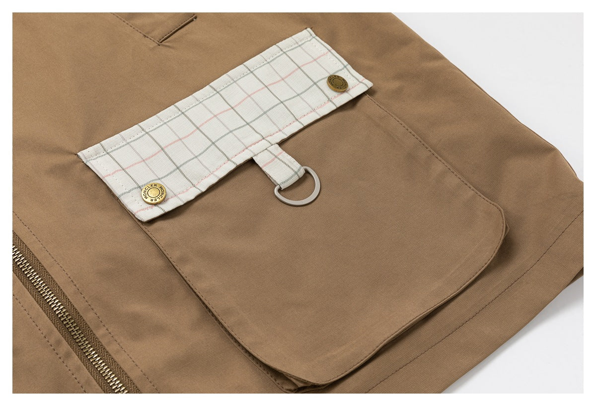 Tan jacket pocket detail with a cream plaid flap, metal D-ring and visible side zipper.