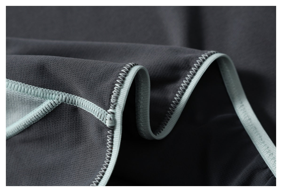 Close-up of charcoal fabric showing pale mint binding and zigzag stitching along a curved edge.