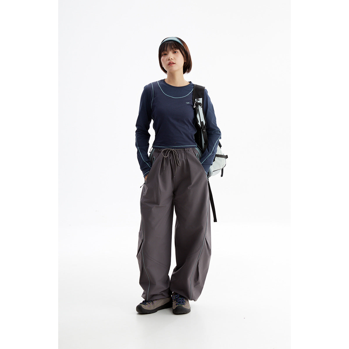 Model wearing a navy long-sleeve top with turquoise piping and charcoal wide-leg pants, with a backpack.