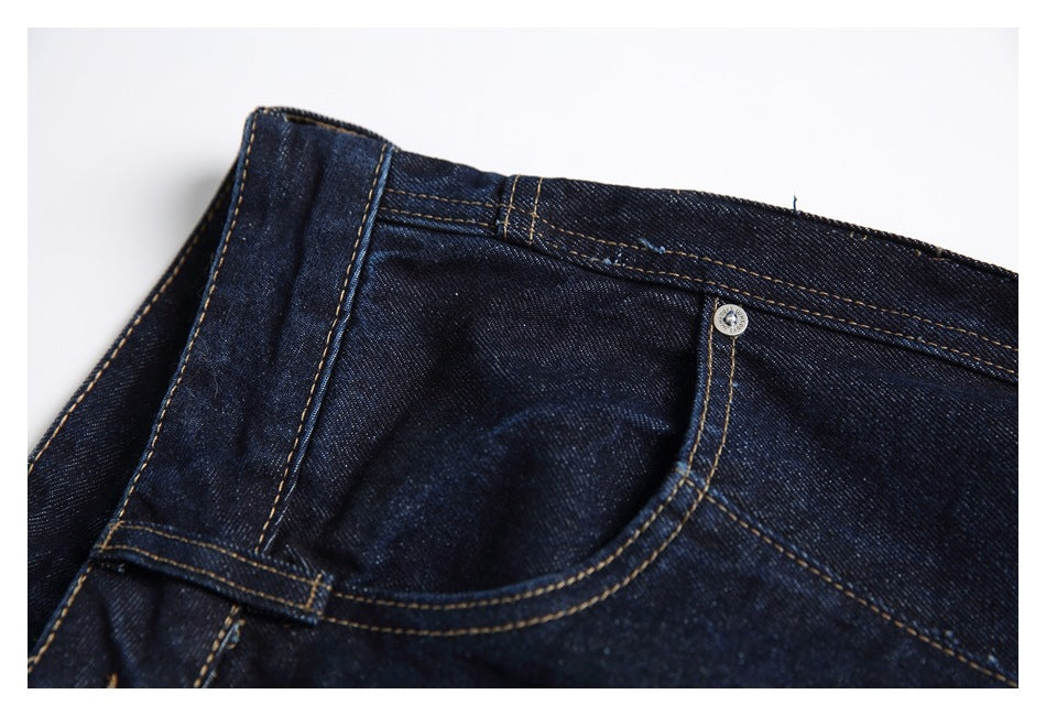 Close-up of a front pocket opening and waistband on dark indigo jeans with tan stitching and a metal rivet.
