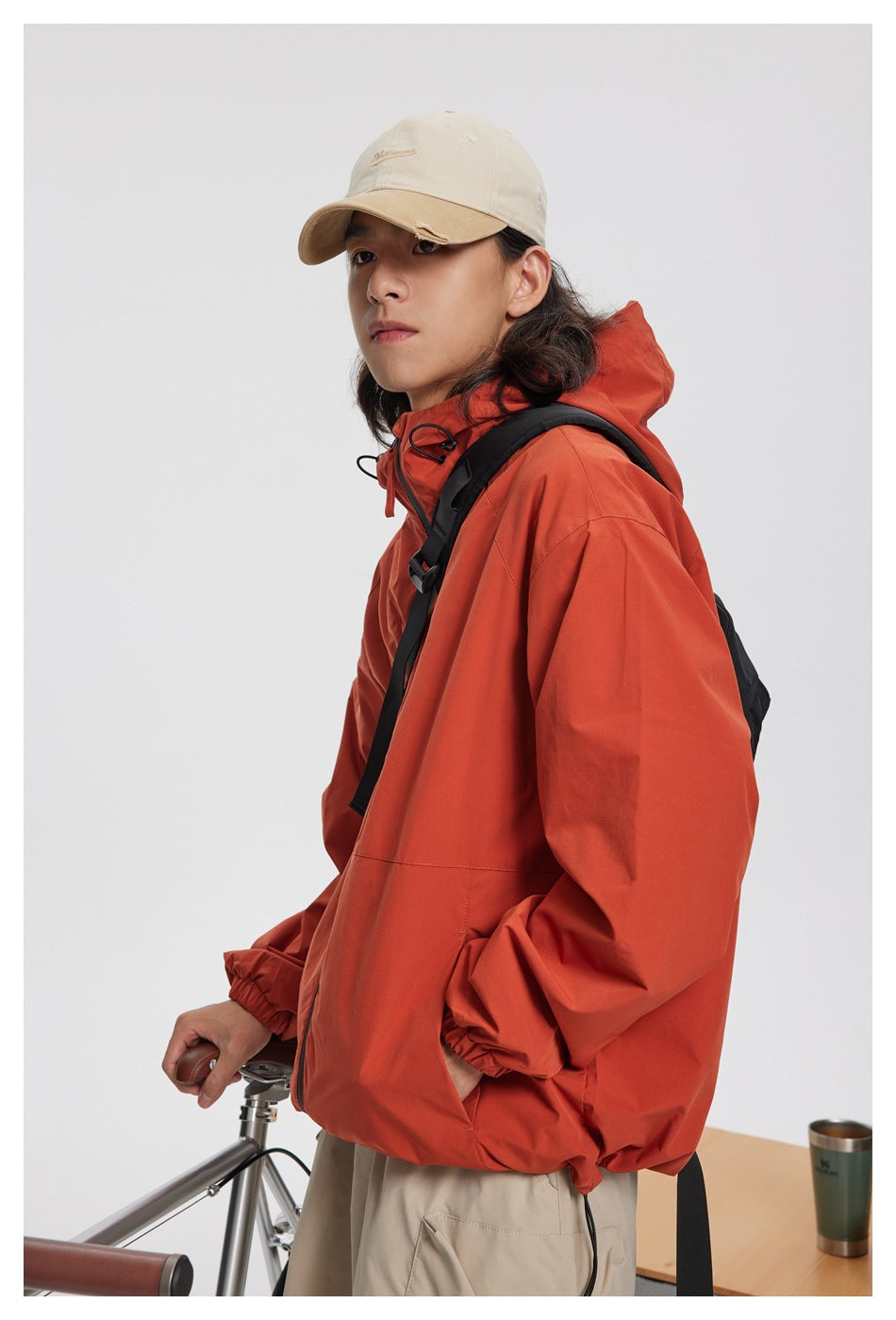 Model wearing a rust-orange hooded jacket with the hood down, shown from the front at an angle.